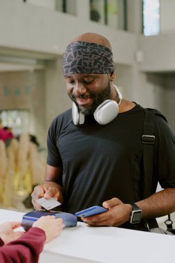 Genç ve iyimser Afro-Amerikan bir adam gümüş kartını takıyor ve elinde telefonunu tutuyor.