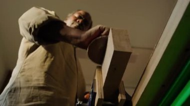 Kara marangozun iş günü ahşap atölyede zımpara ile ahşap bloğu zımparalarken düşük açılı görüntüsü