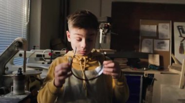 Önlük takan küçük bir çocuğun portresi güvenlik gözlüğü takıyor ve marangozluk dersinde kameraya poz veriyor.
