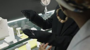 Afrika kökenli Amerikalı bir kadına, kaliteli bir butikten mücevher alan güzel bir platin kolye gösteren kadın satış elemanı.