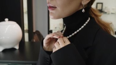 Seçkin bir butikte seçkin beyaz inci mücevherler denerken kolye ve küpeleri beğenen tanınmamış genç bir kadının yakın çekimi.
