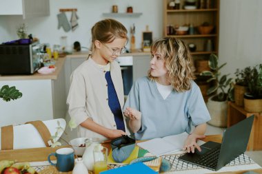 Kafkasyalı hemşire anne ve kız işten önce kahvaltı saatinde okul projesini tartışıyorlar.