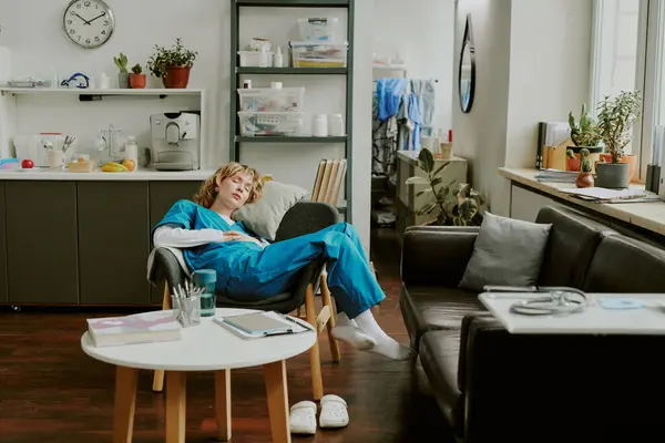 stock image Young Caucasian paramedic sleeping in velvet armchair in recreation zone surrounded by furniture and decor items