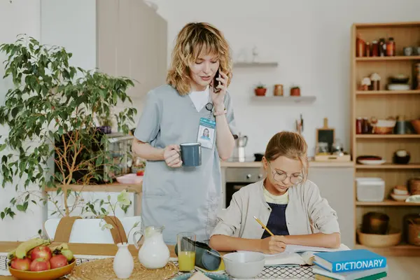 Doktor anne kızlarının ödevlerini kontrol ediyor ve telefonda konuşurken kız da yemek alanında egzersiz yapıyor.