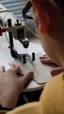 Tahta testereyle odun kesen küçük bir çocuğun tahta işçiliği dersi sırasında el işi projesi üzerinde çalışırken omuz üstü çekilmiş fotoğrafı.