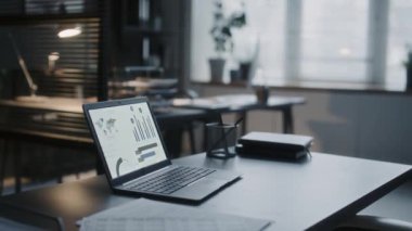 Bilgisayarın modern ofis masasında arkaplanda kalem tutacağı ve not defteri ile veri grafiklerini gösteren yakın plan görüntüsü.