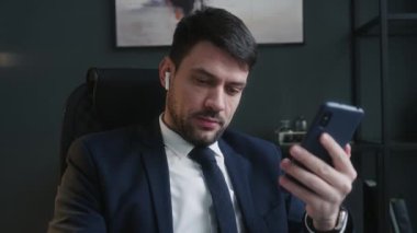 Resmi takım elbiseli genç erkek CEO ofiste iş görüşmeleri sırasında kablosuz kulaklıklarla iş konuşuyor.