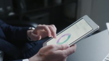 Ofis masasında otururken dijital tablet ekrandaki veri tablolarını karıştıran tanınmayan finansal analistin ellerinin yakın görüntüsü