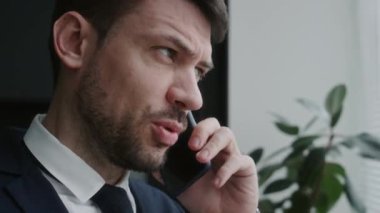 İş günü pencerenin yanında panjurlu duran ve cep telefonuyla konuşan işadamlarının yakın çekim görüntüsü