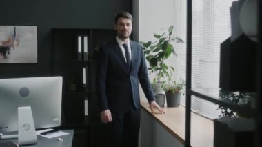 Kendine güvenen şirket CEO 'sunun portresi modern ofisin penceresinin yanında duruyor ve iş günü kameraya poz veriyor.