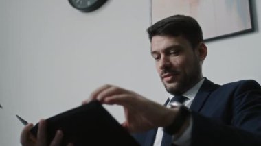 Erkek CEO 'nun resmi takım elbise giymesi, iş belgelerini gözden geçirmesi ve ofisteki meslektaşıyla konuşması düşük açılı bir bakış açısı.