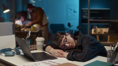 Genç beyaz kadın yöneticinin bilişim şirketinde masa başında kestirirken, meslektaşlarının son teslim tarihiyle ilgili yazılım projesinde çalışırken çekilmiş bir zaman çizelgesi.