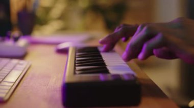 Ev kayıt stüdyosundaki masasında renkli neon ışıklarıyla dolu klavye kullanan tanınmayan erkek müzisyenlerin ellerinin yakın görüntüsü