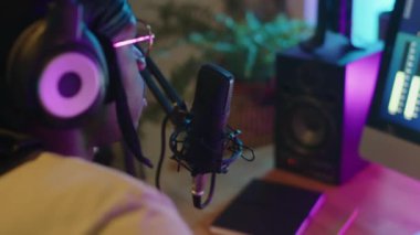 Afrika kökenli Amerikalı şarkıcının kulaklıklarıyla dijital ses istasyonunda otururken ve mikrofon içinde neon ışıklı müzik kaydederken yakın plan çekimleri.