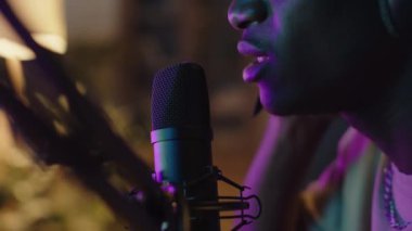 Ev kayıt stüdyosundaki renkli neon ışıklı mikrofonda şarkı söyleyen siyahi müzisyenin yakın çekim görüntüsü