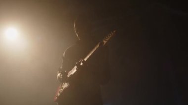 Afrika kökenli Amerikalı gitaristin silueti sisli sahnede arka planda solo performans sergiliyor.