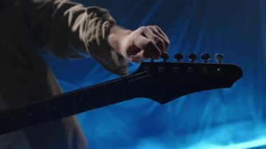 Sahnede, mavi arka plan ışıklandırmalı elektro gitarın ayarlarını ayarlayan müzisyenin yakın çekim görüntüsü