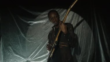 Afrika kökenli Amerikalı gitarist, loş ışıklandırma sahnesindeki rock müzik konserinde parlak arka plan ve flaş ışığı eşliğinde elektro gitar çalıyor.