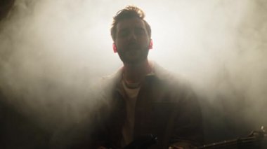 Genç erkek sanatçı sisli sahnede sahne arkasında duruyor, gitar çalıyor ve müzik konserinde şarkı söylüyor.