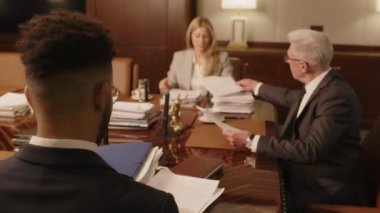 Kıdemli, kır saçlı hukuk firması lideri, yönetim kurulundaki toplantıda yanında oturan iki meslektaşına belge veriyor.