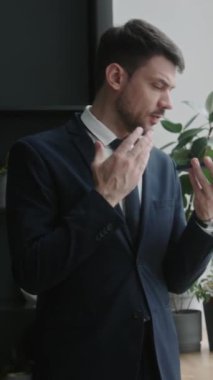 Ofisin penceresinde duran resmi takım elbiseli profesyonel işadamının dikey çekimi ve cep telefonuyla sesli mesaj kaydediyor.