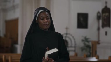 Siyah bornozlu Afro-Amerikan rahibenin Katolik kilisesinde kutsal incille yürümesini.