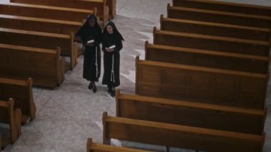 Uzun siyah cüppeli iki Katolik manastırın sabah namazından sonra katedralde kutsal kitaplarını tutarken yüksek açılı görüntüsü.