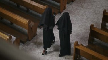 Uzun siyah cüppeli iki Katolik rahibenin kilisedeki mihrabın koridorlarından geçişi.