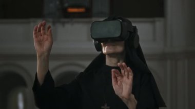 Siyah cüppeli modern rahibenin kilisede sanal gerçeklik gözlüklerini test ederken orta boy fotoğrafı.