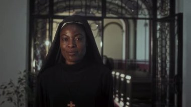 Siyahi dindar kız kardeşin orta boy portresi göğsünde haçla kiliseye gülümseyen kameraya bakıyor.