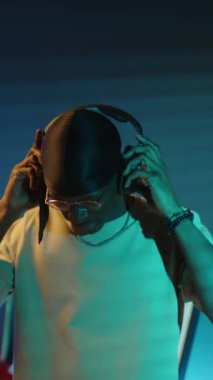 Afro-Amerikalı müzisyenin dikey portresi. Kulaklıklarını çıkarıyor ve neon ışıklı odada kameraya bakıyor.