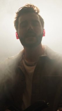 Erkek şarkıcının sisli sahnede arka ışığa karşı durduğu ve müzik konseri sırasında şarkı söylediği dikey çekim.