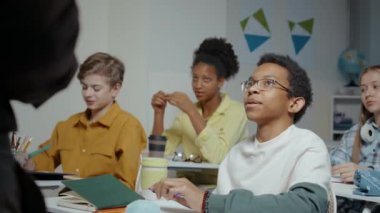 Sınıfta masalarında otururken tanınmayan erkek öğretmenle yeni konu üzerine tartışan bir grup genç öğrencinin orta boy fotoğrafı.