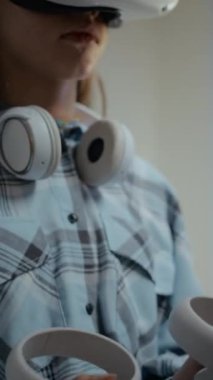 VR kulaklık takan ve elinde sanal gerçeklik deneyimi olan bir çift hareket kontrol cihazıyla tanınmayan genç kızın dikey yakın çekimi.