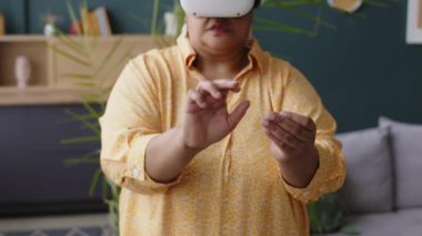 Siyah son sınıf bayan oyun ayarları sanal gerçeklik gözlüğü takıyor oturma odasında duruyor.