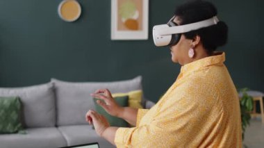 Evde sanal gerçeklik gözlüğü takarak oyun oynamayı seçen siyahi son sınıf öğrencisi kadın.