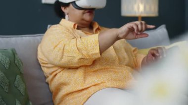 VR gözlüklü Afrikalı Amerikalı son sınıf öğrencisi kadın oturma odasındaki kanepede otururken sanal klavyede daktilo kullanıyor ve arttırılmış gerçeklikte uygulamayı kullanıyor.