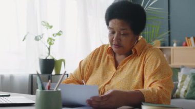 Oturma odasında evrak dolduran siyahi bir bayan. Faturalarını evde ödüyor.