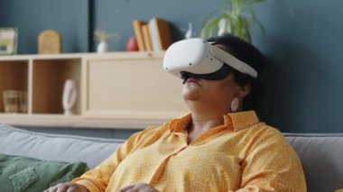 Siyah, yaşlı bir kadın kanepeye oturmuş, kulaklık takıp etrafa bakıyor.