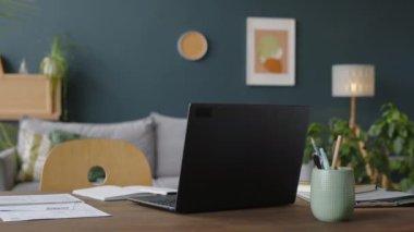 Laptop, faturalar, klasörler, defterler ve kırtasiye kupası modern oturma odasındaki insanların olmadığı masada.