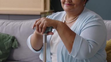 Oturma odasındaki kanepede elleri baston üzerinde oturan gülümseyen Afrikalı Amerikalı son sınıf öğrencisinin portresi.