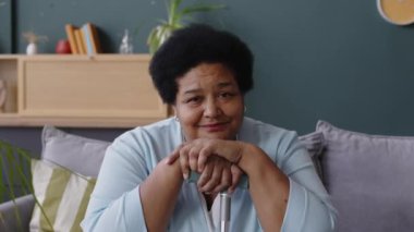 Afro-Amerikan son sınıf öğrencisinin oturma odasındaki kanepede otururken elini bastona uzattığı ve çenesini onlara dayadığı fotoğrafı.