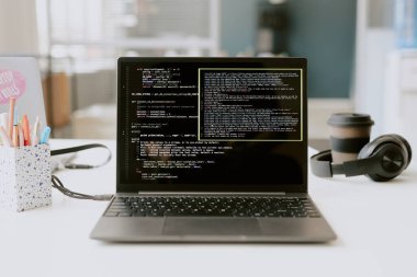 Siyah kulaklıklardan, ofis malzemelerinden ve gümüş dizüstü bilgisayarın yanındaki kahve fincanından oluşan orta ölçekli bir program başlatıldı.