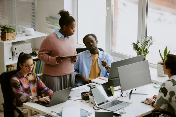 stock image African American colleagues discussing last report and looking at screen while their Caucasian coworker writing code