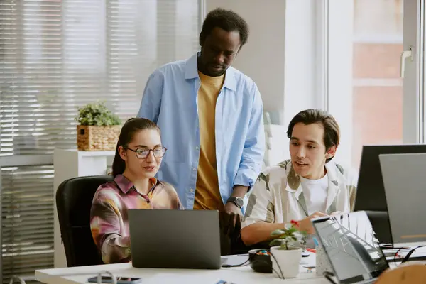 stock image African American teamlead standing between two Caucasian coworkers who showing new project to him