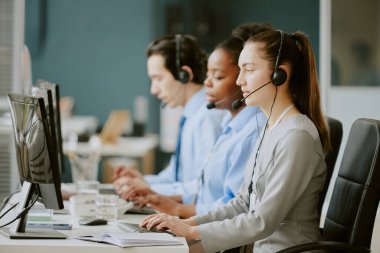 Genç melez çağrı merkezi operatörleri çalışma masasında elektronik cihazlar ve ofis malzemeleriyle modern ve rahat ofis malzemelerinin üstünde oturuyorlar.