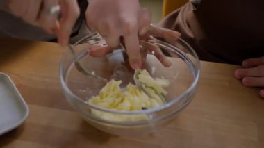 Mutfak masasında birlikte yemek pişirirken iki tanınmayan kadının tereyağını çatalla cam kasede ezmelerini yakından izleyin.