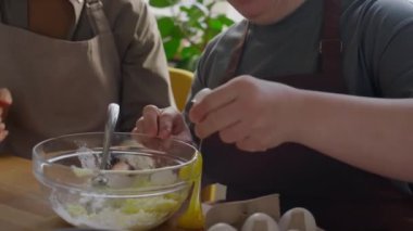 Down sendromlu bir kız yemek kursunda ona yardım ederken kaseden yumurta kırıyor ve gülümsüyor.