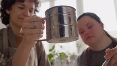 Down sendromlu bir kız yemek kursunda cam kasede yemek pişirirken kadın öğretmenin un ellemesini yakından izleyin.