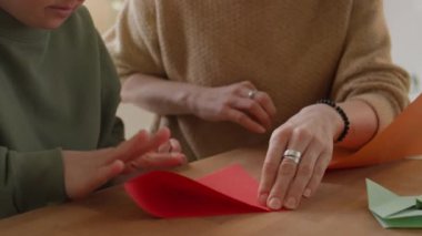 Sanat ve zanaat dersinde birlikte origami yaparken Down sendromlu bir kız ve kadın öğretmenin masasında renkli kağıtları katlamasına yakından bakın.
